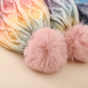 Close-up of tie-dye gradient knit hat featuring thick cable texture and a fluffy pom-pom