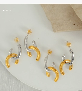 Close-up of geometric twist earrings in gold and silver finish on a white stone tray