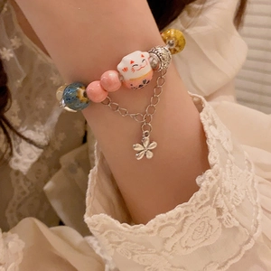 Cute ceramic maneki neko cat beaded bracelet with floral charms on a female wrist