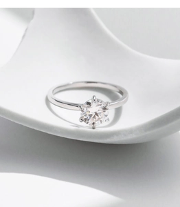 Detailed view of 1 carat round moissanite ring with six-prong setting on white ceramic