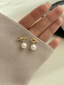 Detail of elegant gold knot earrings with white lustrous pearls held by fingers