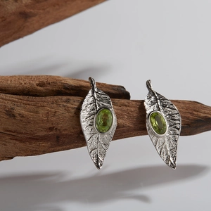 Macro detail of leaf-shaped silver earrings with oval green gemstones on wood