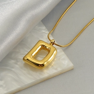 Detail of gold bubble letter D pendant with glossy snake chain on elegant silk background