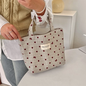 Détail du sac à lunch en toile avec broderie nœud rouge et motif à carreaux tenu par modèle