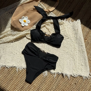 Dettaglio in piano del bikini nero a due pezzi con anelli in metallo a cuore dorato su stuoia