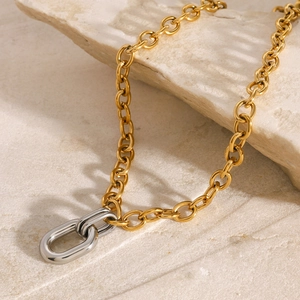 Detail of two-tone gold chain with interlocking silver rings on a stone surface