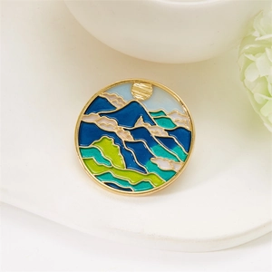 Detail view of round enamel mountain landscape brooch with gold frame on white tray