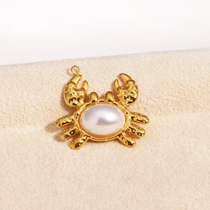 Close-up of a gold crab pendant with a white pearl inlay on a soft beige fabric