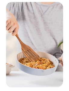 Close-up of a slotted teak wood spatula stir-frying food in a white ceramic pan