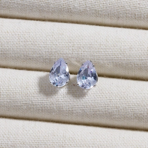 Macro shot of silver teardrop earrings with clear sparkling zircon stones on fabric