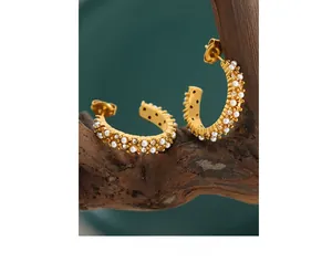 Détail macro de boucles d'oreilles en or 18K avec perles et zircons sur bois
