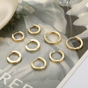Detail of four pairs of polished 18K gold hoop earrings on beige silk fabric background