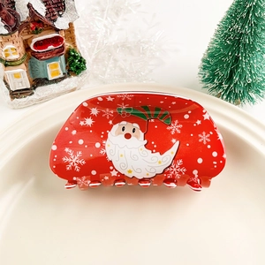 Pince à cheveux rouge de Noël avec motif Père Noël et flocons sur une assiette blanche