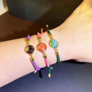 Detail of adjustable braided rope bracelets in purple, pink and green with gold charms
