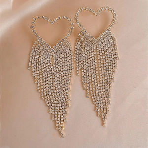 Detailed close-up of golden heart-shaped fringe earrings with rhinestones on silk fabric