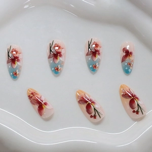 Faux ongles amande à motif floral avec dégradé bleu et orange sur plateau blanc