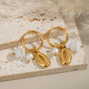 Détail de boucles d'oreilles dorées avec breloques coquillage, perle et pierre blanche
