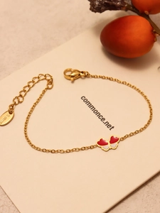 Détail d'un bracelet papillon doré avec émail rouge et blanc sur carte cadeau