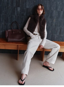 Fashion detail of brown faux fox fur vest styled with beige knitwear and tote bag