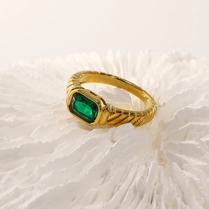 Macro detail of French style 18k gold ring with ribbed texture and emerald-cut green stone