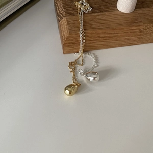 Detailed view of highly polished gold and silver water drop pendants on minimalist chains