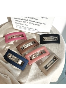 Flat lay of six matte rectangular hair clips in assorted Morandi colors on linen fabric