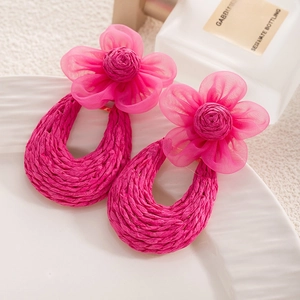 Close-up of pink raffia and mesh flower earrings with woven textures on a white plate