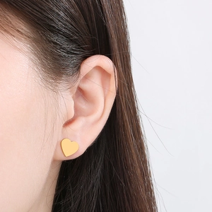 Close-up of a woman wearing gold heart-shaped stud earrings in a minimalist style