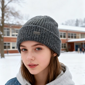 Dark grey knitted beanie for men and women with metal logo tag in winter snow setting