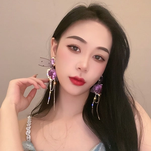 Detailed view of long purple crystal heart earrings with silver tassels on model