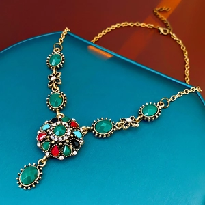 Detail of vintage flower necklace featuring green stones and multicolor crystals on a blue stand
