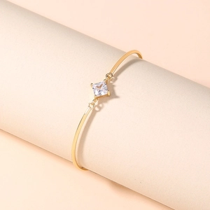Macro detail of gold-plated bangle featuring a square-cut sparkling zircon on a stand