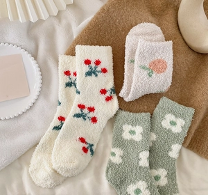Close-up of cozy coral fleece socks with cherry and peach patterns on a soft plush blanket