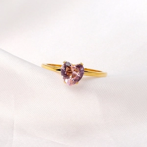 Golden 18K stainless steel ring with heart-shaped pink gem on white silk background