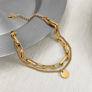 Detail of a double-layer gold chain bracelet featuring a sleek circular pendant on a disc