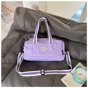 Detail of purple cylindrical dance bag with adjustable straps on a gray sofa