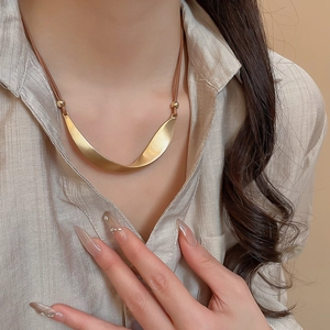 Detail of twisted gold metal pendant on brown cord necklace worn with beige shirt