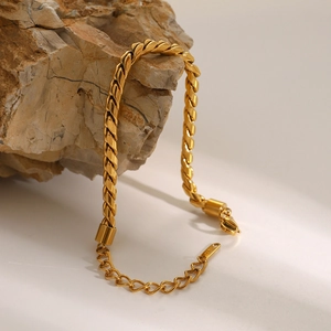 Macro detail of gold twisted rope chain bracelet with 18K tag on natural stone