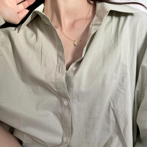 Close-up of minimalist golden oval pebble pendant on necklace worn with green shirt