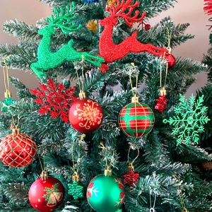 Dettaglio di ornamenti a forma di renna rossi e verdi sui rami innevati dell'albero