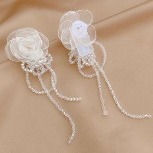 Detail of white organza rose earrings with long crystal beaded tassels on silk background
