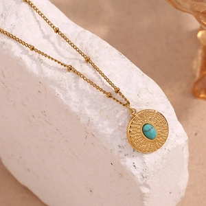 Detail of 18K gold-plated beaded chain and hammered turquoise pendant on stone