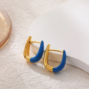 Detailed view of U-shaped gold earrings with blue enamel finish on minimalist props