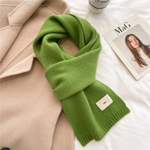 Detail of green knit scarf with ribbed texture and small beige label on soft coat