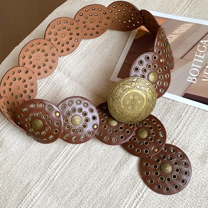 Detailed close-up of a caramel brown leather belt with brass floral embossed buckle