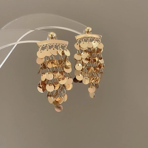Detailed view of gold tiered disc tassel earrings on a transparent acrylic stand