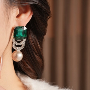 Primo piano di orecchino vintage con gemma verde, montatura in argento e perla grande