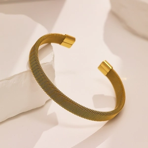 Detailed macro view of the gold mesh texture on a stainless steel open cuff bracelet