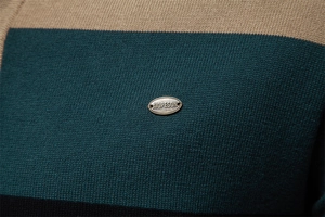 Detail von gestreiftem Strickstoff in Khaki und Grün mit metallener Logoplakette