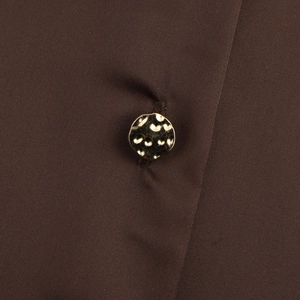 Gros plan d'un bouton doré texturé sur le tissu lisse d'une chemise marron foncé
